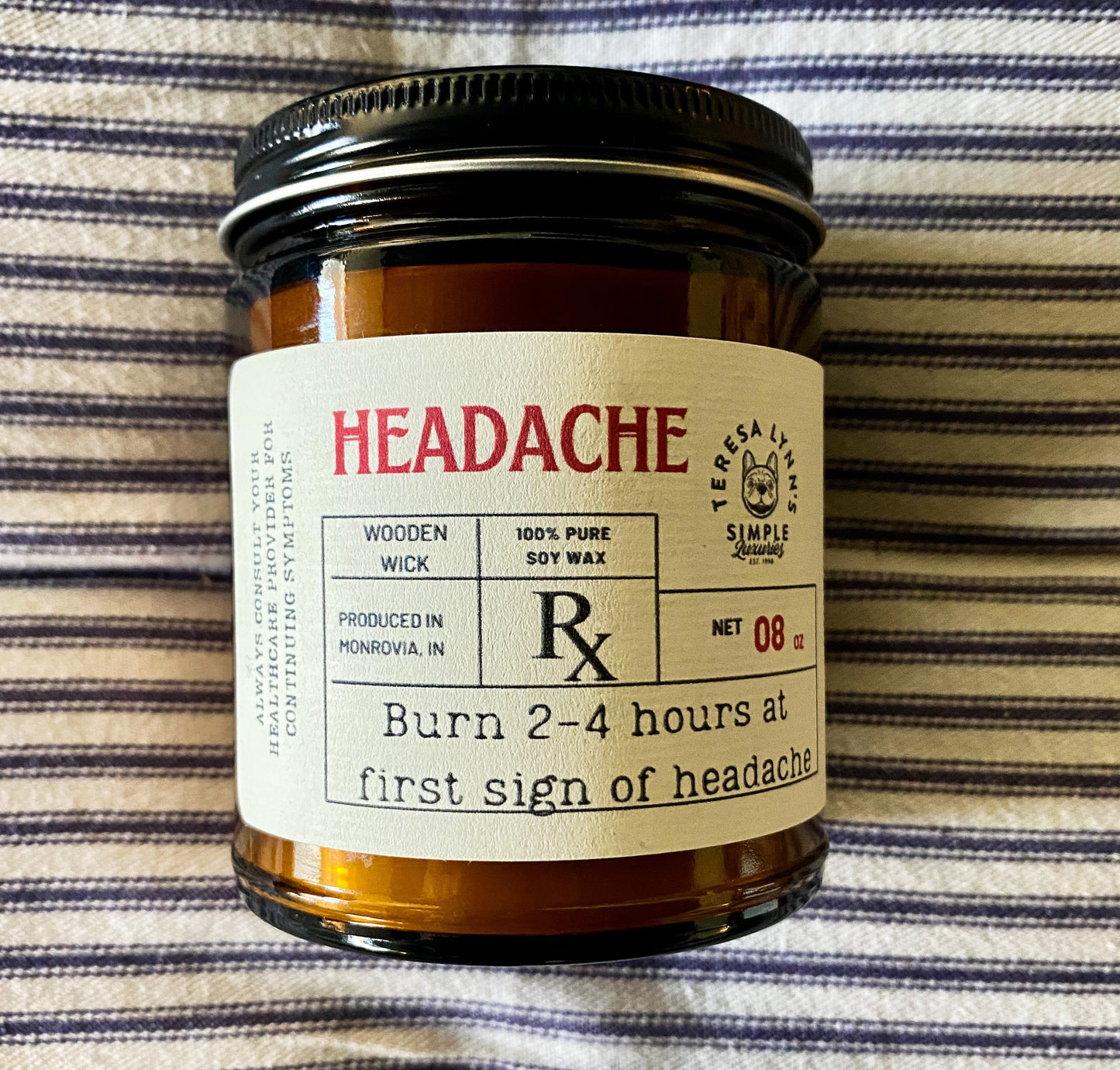 A 9oz brown glass apothecary style candle jar with a black lid. The label is designed to look like a vintage prescription label with the word Headache at the top in red antique font.