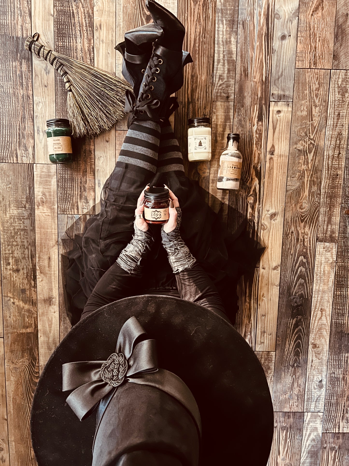 Image of Teresa sitting on the floor.  She is wearing a handmade witches hat, a toile skirt, black and grey striped stocking, pointy lace up velvet and leather boots.