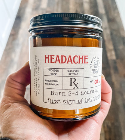 Headache, wooden wick, aromatherapy candle, soy wax candle - The Preachers Daughter Candle Co
In Teresas Hand sits a 9oz brown glass apothecary style candle jar with a black lid.  The label is designed to look like a vintage prescription label with the word Headache at the top in red antique font.